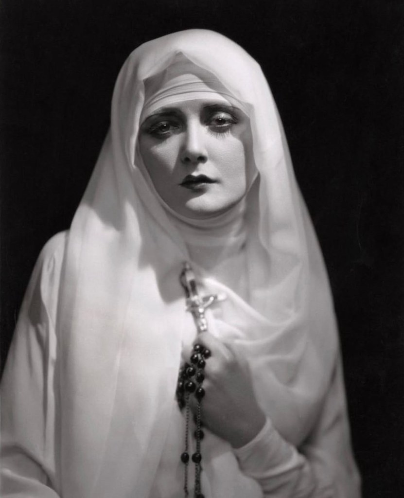 Publicity shot of Mary Nolan in Mary Nolan in Memoirs of a Nun, 1927. She wears a white habit and holds rosary beads.