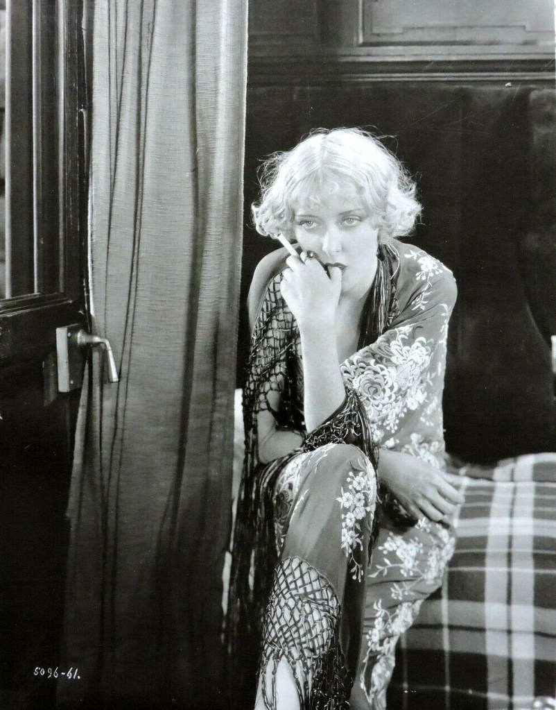 Mary Nolan in Shanghai Lady, 1929. She is shown sitting on a bed, smoking a cigarette.