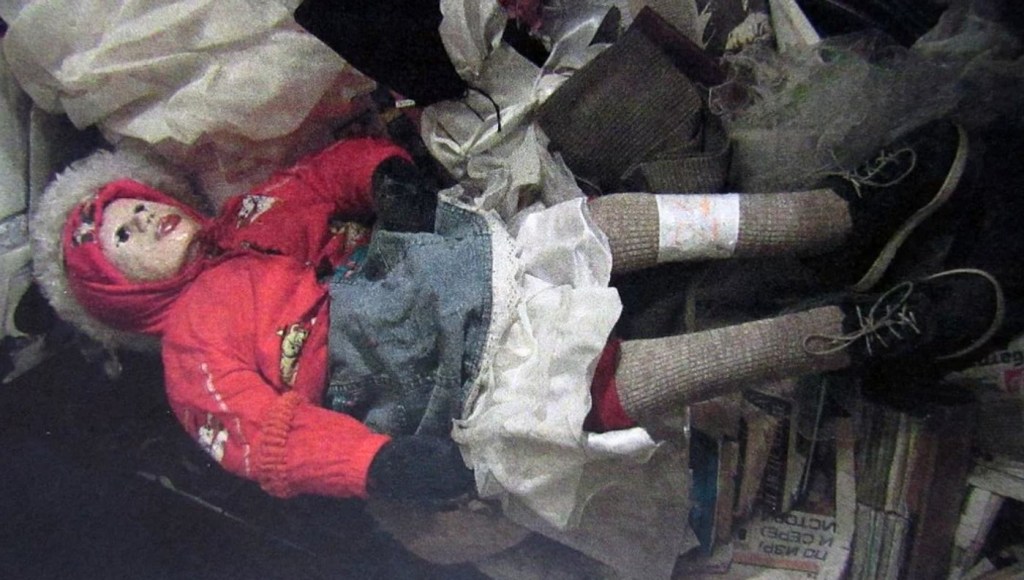 The mummified body of a child found in Anatoly Moskvin's apartment. The body is dressed in a pink jacket and a white frilly dress, and make up has been applied to the face.
