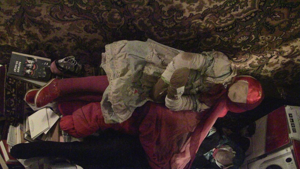 The mummified body of a child found in Anatoly Moskvin's apartment. The body is dressed in a pink ski suit and black patent leather boots. The face is covered by what appears to be black nylon fabric.